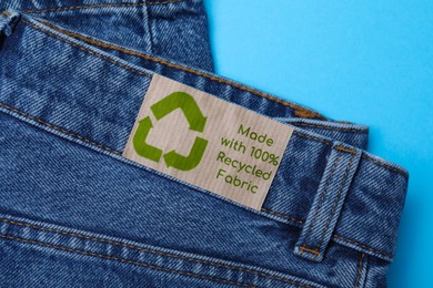 Jeans with recycling label on light blue background, closeup