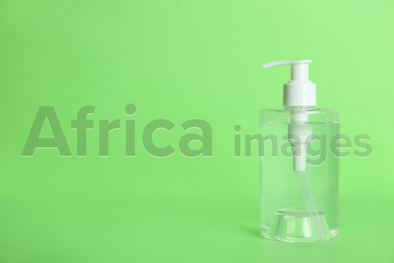Dispenser bottle with antiseptic gel on green background. Space for text