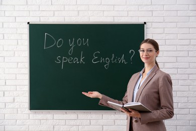 Photo of Teacher near green chalkboard with inscription Do You Speak English? in classroom