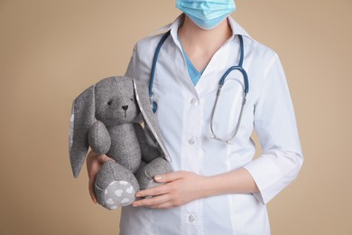 Pediatrician with toy bunny and stethoscope on beige background, closeup