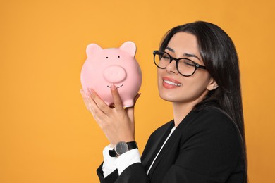 Photo of Young woman in eyeglasses with piggy bank on orange background