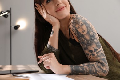 Photo of Beautiful woman with tattoos on arm at table indoors, closeup