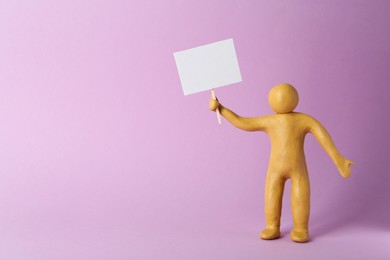 Human figure made of yellow plasticine holding blank sign on violet background. Space for text
