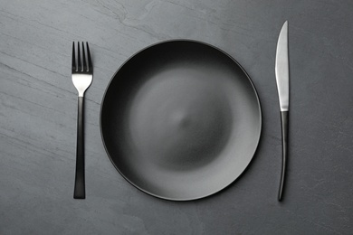 Stylish ceramic plate and cutlery on dark background, flat lay