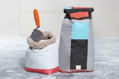 Photo of Cement powder in bags and trowel on stone floor
