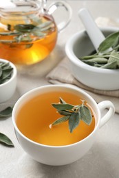 Cup of sage tea with green leaves on white table