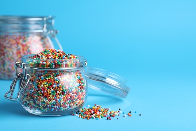Colorful sprinkles and jar on light blue background, space for text. Confectionery decor