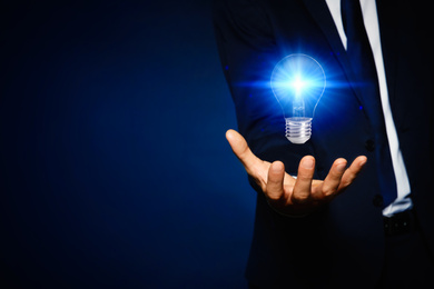 Idea concept. Businessman with glowing light bulb on dark background, closeup