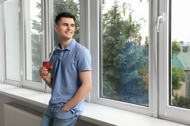 Handsome young man with glass of juice near window at home