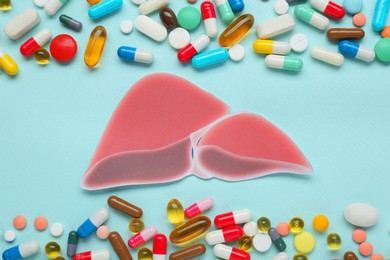 Photo of Paper liver and pills on turquoise background, flat lay. Hepatitis treatment
