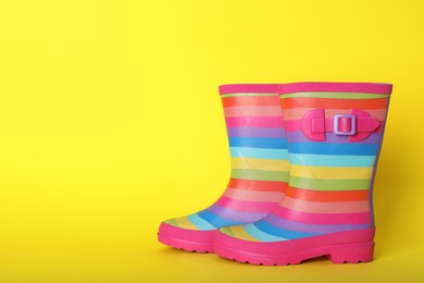 Pair of striped rubber boots on yellow background. Space for text