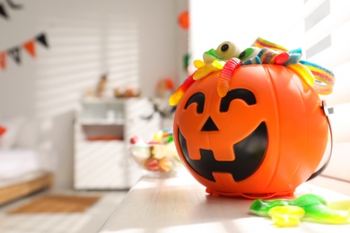 Halloween trick or treat bucket with different sweets near window indoors
