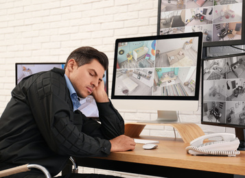 Male security guard sleeping near monitors at workplace