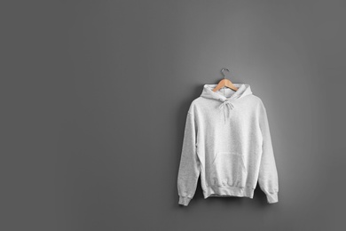 Photo of New hoodie sweater with hanger on grey wall. Mockup for design