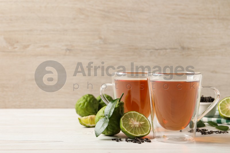 Photo of Glass cups of tasty bergamot tea and fresh fruits on white wooden table, space for text