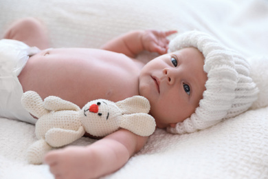 Cute newborn baby with toy in white knitted hat on plaid