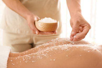 Young woman having body scrubbing procedure with sea salt in spa salon, closeup