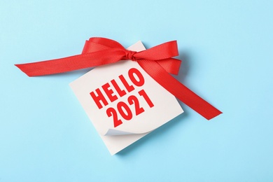Memory stickers with text HELLO 2021 and red bow on light blue background, top view