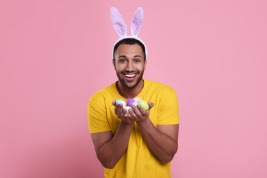Photo of Happy African American man in bunny ears headband with Easter eggs on pink background