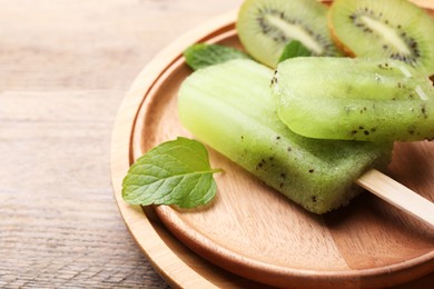 Plate of tasty kiwi ice pops on wooden table, closeup. Fruit popsicle