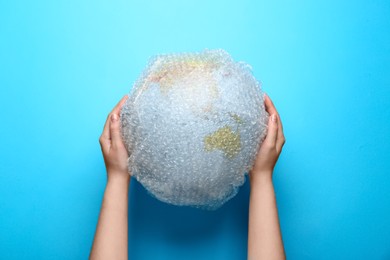Photo of Woman holding globe packed in bubble wrap on turquoise background, top view. Environmental conservation