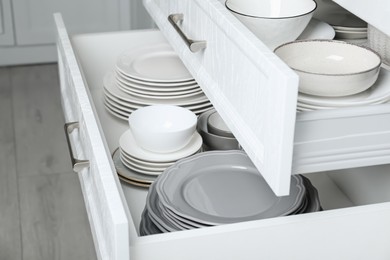 Photo of Open drawers with different plates and bowls in kitchen, closeup
