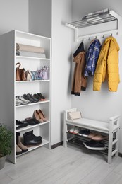 Photo of Shelving unit, coat rack and shoe storage bench near white wall in hallway. Interior design