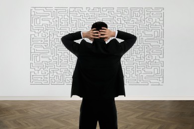 Image of Businessman looking at wall with illustration of maze indoors