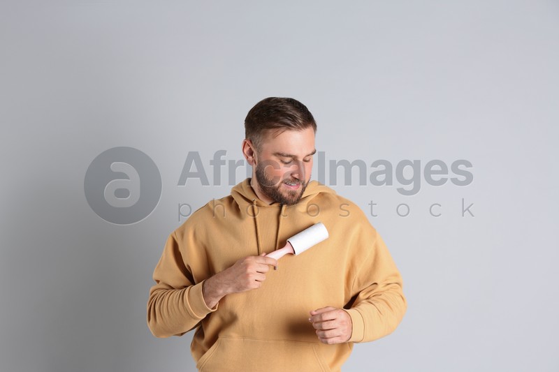 Photo of Young man cleaning clothes with lint roller on grey background