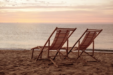 Photo of Wooden deck chairs on sandy beach at sunset. Summer vacation