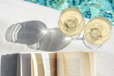 Photo of Glasses of tasty wine and open book on swimming pool edge, above view