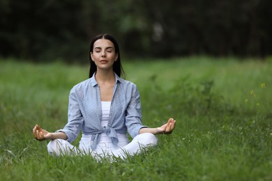 Young woman meditating on green grass. Space for text