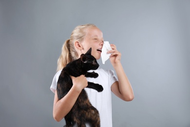 Photo of Little girl with cat suffering from allergy on grey background