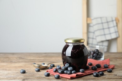 Photo of Jar of blueberry jam and fresh berries on wooden table. Space for text