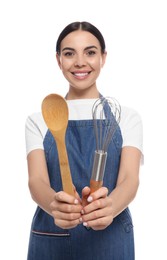 Young woman in blue jeans apron holding wooden spoon and whisk on white background