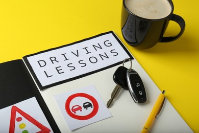Workbook for driving lessons, cup of coffee and keys on yellow background. Passing license exam