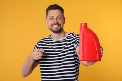 Man pointing at motor oil against orange background, focus on hand container