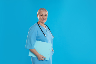 Mature doctor with stethoscope and clipboard on blue background. Space for text