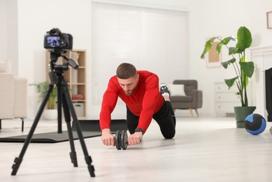 Photo of Trainer with ab wheel recording workout on camera at home