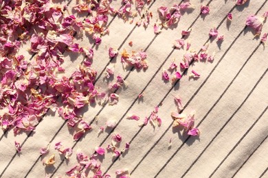 Scattered dried tea rose petals on striped fabric, top view