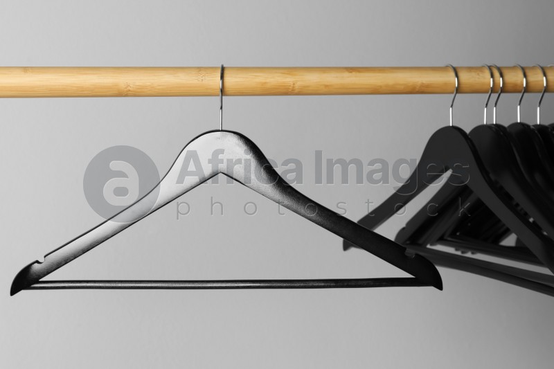 Photo of Black clothes hangers on wooden rail against light grey background