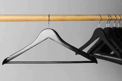 Black clothes hangers on wooden rail against light grey background