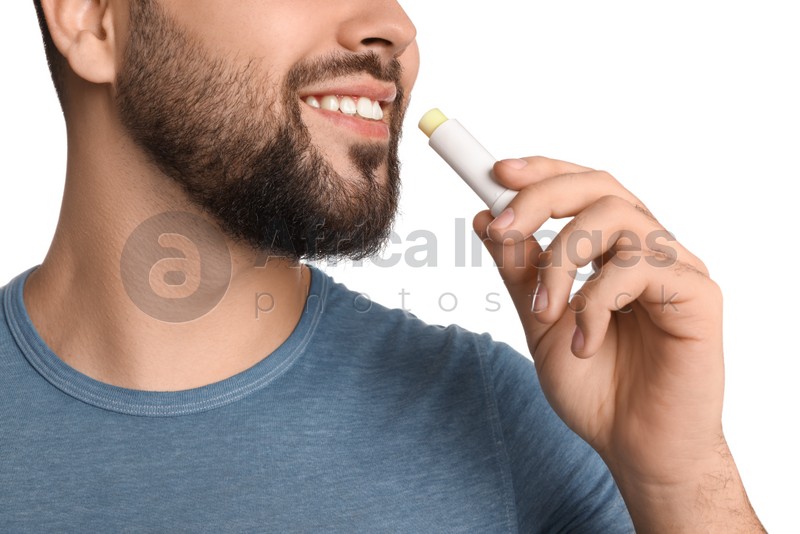 Young man applying lip balm on white background, closeup