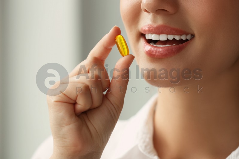 Young woman taking dietary supplement pill on blurred background, closeup