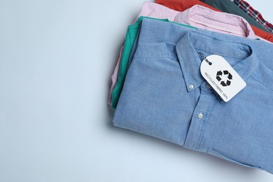 Stack of clothes with recycling label on light background, top view. Space for text