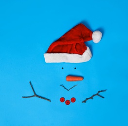 Creative snowman shape made of Santa hat and different items on light blue background, flat lay
