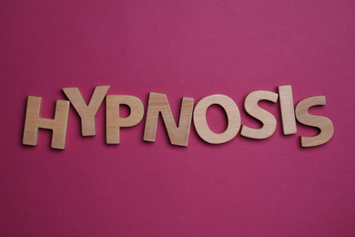 Word HYPNOSIS made with wooden letters on magenta background, flat lay