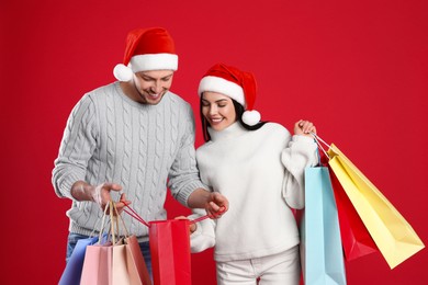 Happy couple with paper bags on red background. Christmas shopping