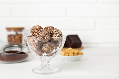 Photo of Glass dessert bowl of tasty chocolate balls on white wooden table, closeup. Space for text