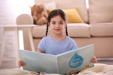 Little girl with chickenpox reading book at home